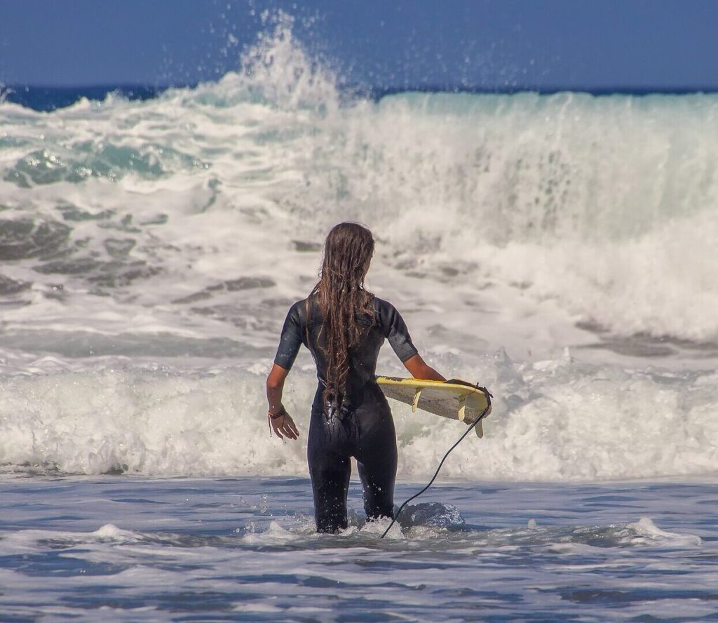 Surfer girl with long hair walking into the water holding a surfboard at Sunshine Coast Surf