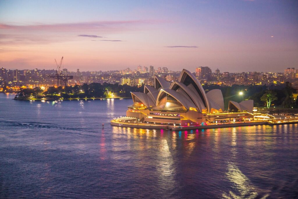 Sydney Opera House illuminated at night, with vibrant pink and purple skies above and the Sydney skyline