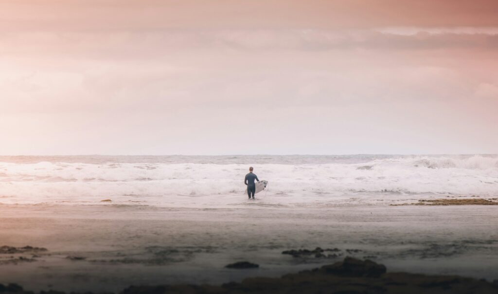 Surfer entering the ocean at Kings Beach, Caloundra Surf, with pink and grey skies, waves