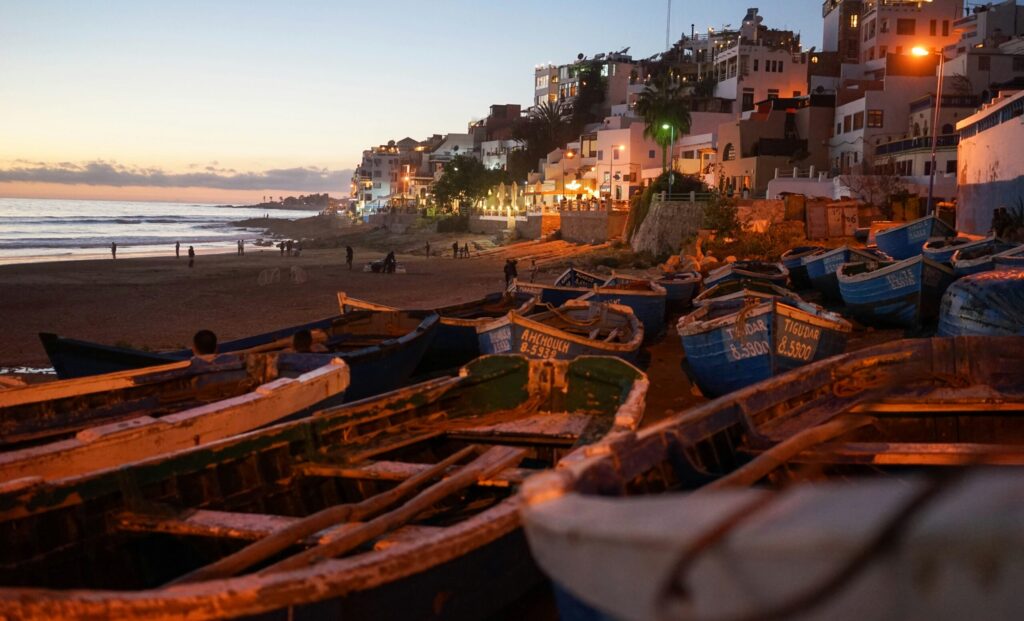 Taghazout Beach, Morocco, features boats in the foreground and illuminated apartments in the background