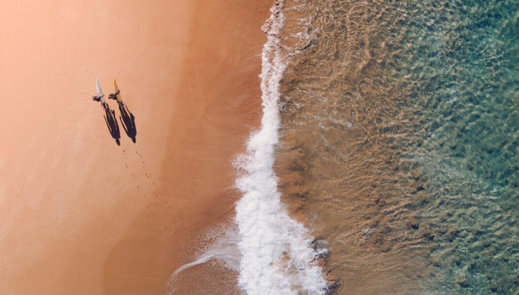 A bird's-eye view of two people walking side by side with surfboards on a golden sandy beach at Puerto Viejo Costa Rica