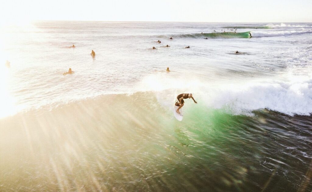 Surfer executing a backhand turn with sunlight reflecting off the waves, surrounded by surfers Burleigh Point, Gold Coast