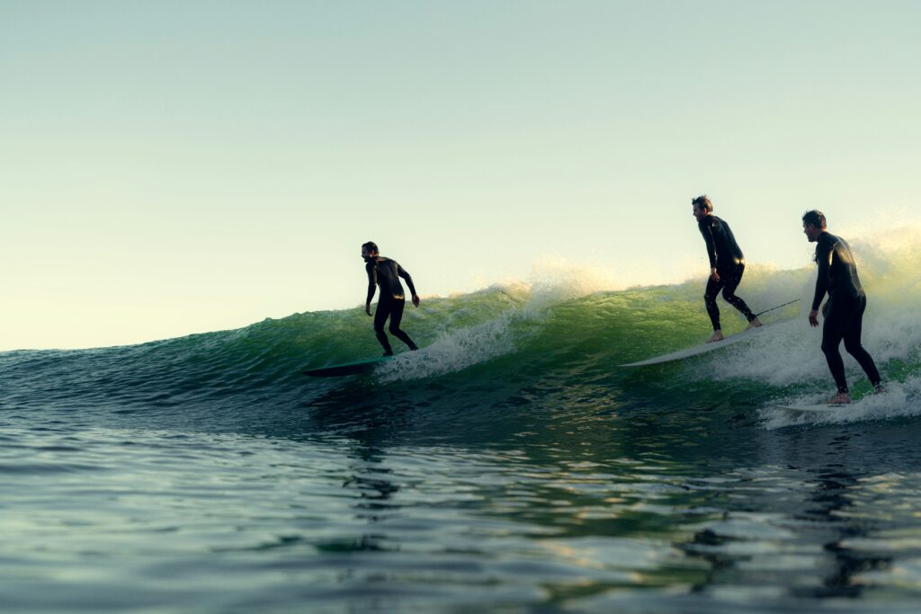 Three men surfing longboards on a right-hand wave under clear blue skies, gliding in sync across the ocean's surface