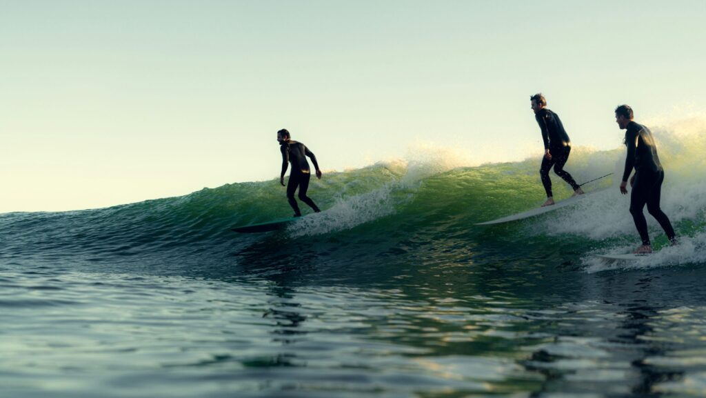 Three men surfing longboards on a right-hand wave under clear blue skies, gliding in sync across the ocean's surface