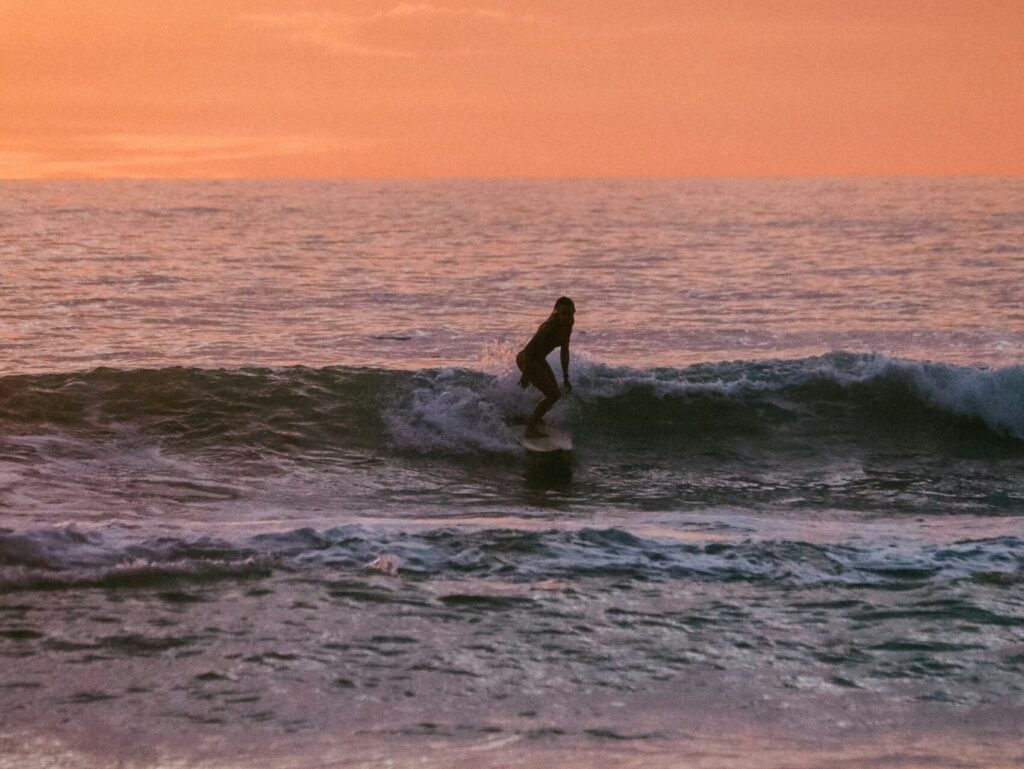 A girl surfing a small wave under a vibrant yellow and orange sky, capturing the beauty of the sunset as she glides across the water