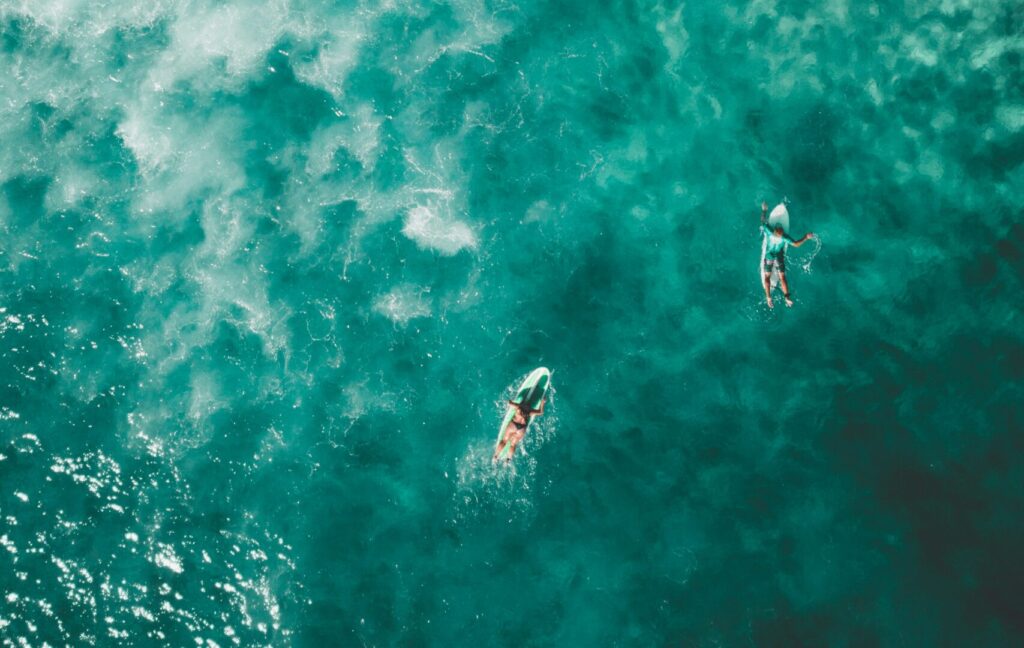 Bird's eye drone view of Bondi Beach Surf, Sydney, showcasing three surfers paddling in the vibrant blue water