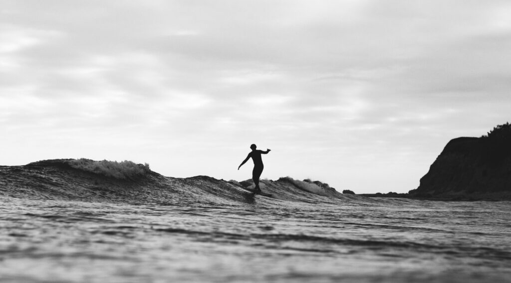 A black and white photo of a man hanging five on a surfboard, captured from the water at Puerto Viejo Surf, Costa Rica