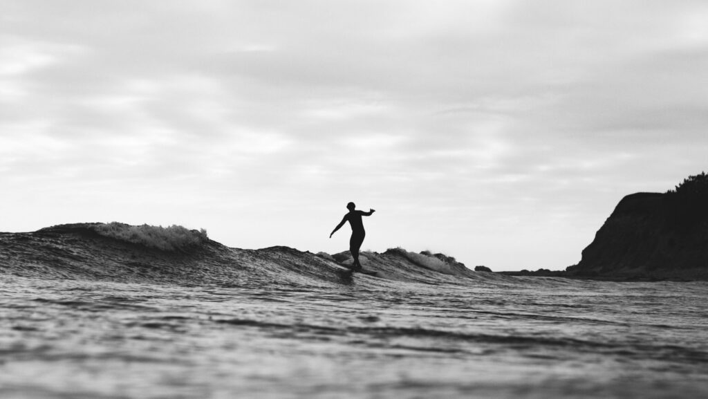 A black and white photo of a man hanging five on a surfboard, captured from the water at Puerto Viejo Surf, Costa Rica