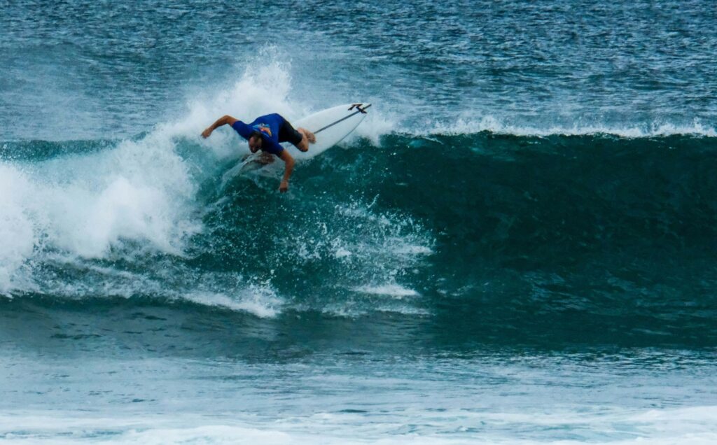 Surfer executing a powerful backhand turn on a left-hand wave at Hikkaduwa Surf Main Reef, with vibrant blue water