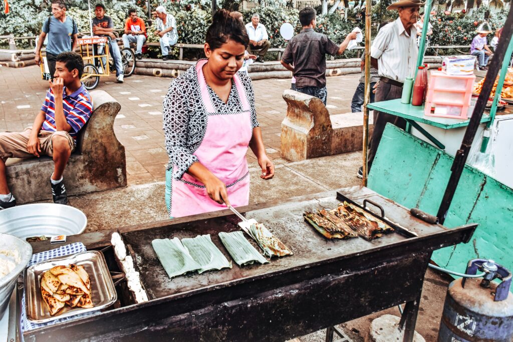 A lady cooking street food in San Salvador, El Salvador, with people in the background, capturing the vibrant atmosphere of the market