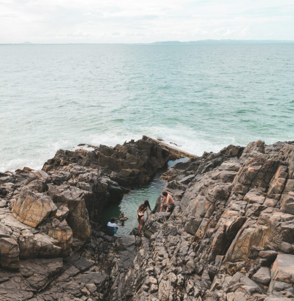 People swimming in the natural rock pools formed by the ocean at Noosa National Park