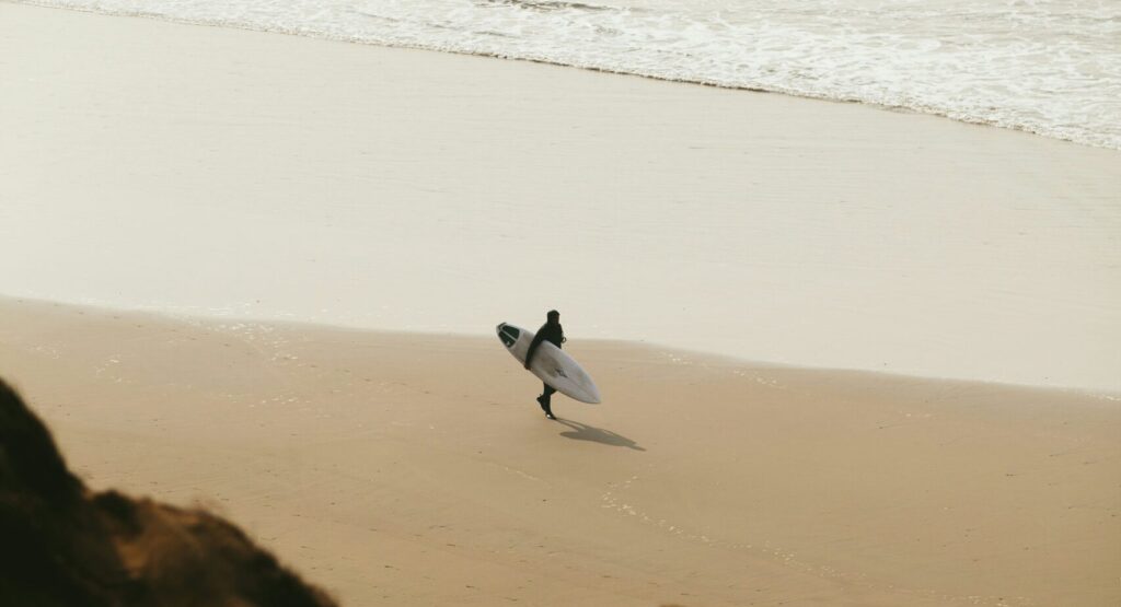 A surfer walking along the beach, captured from atop a sand dune