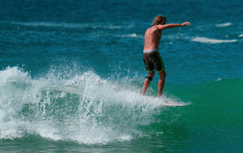 A surfer riding a longboard near the front of the wave at Hiriketiya Surf Beach, showcasing vibrant blue water