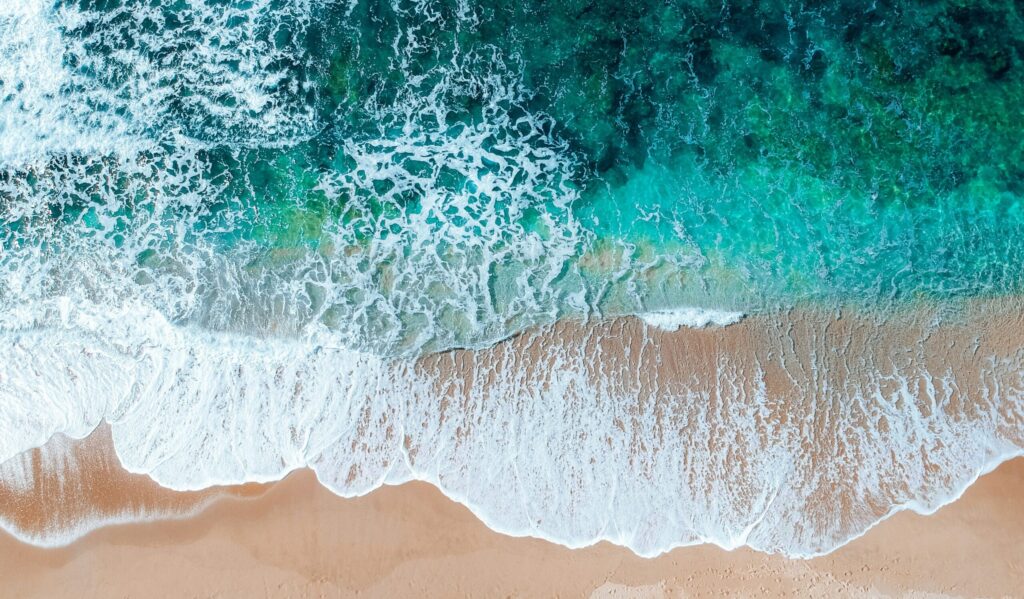 Bird's eye drone view of Kings Beach, Caloundra, showcasing golden sand and vibrant blue water under clear skies