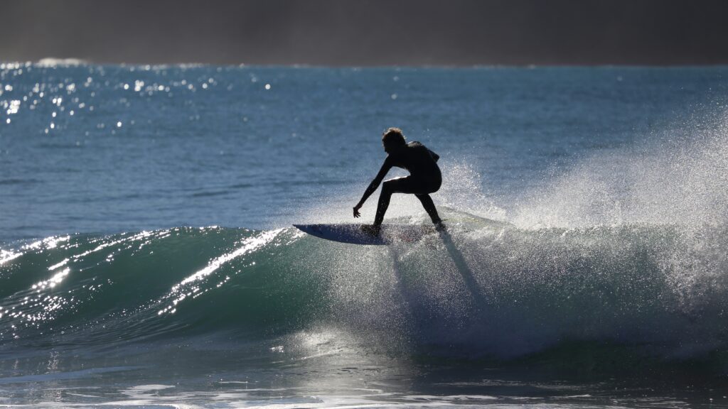 A surfer performing a floater above a wave, with bright blue water and sunshine creating a vibrant, energetic atmosphere