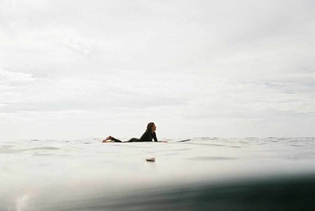 A girl lying on a surfboard in the ocean, captured with a cloudy sky above and calm water surrounding her, creating a serene atmosphere