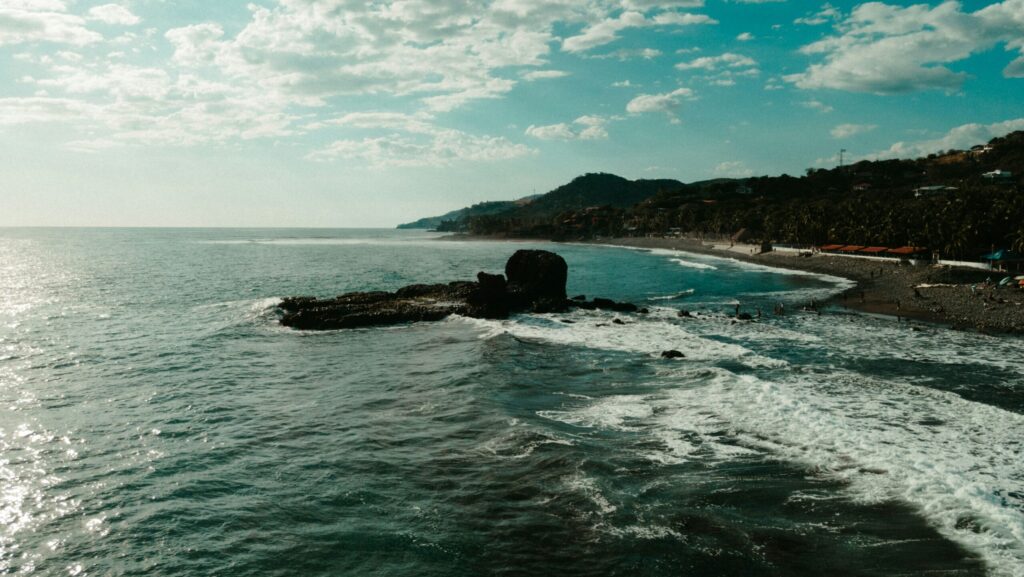 A drone photo of El Tunco surf, El Salvador, showcasing the ocean and beach, with surrounding hills
