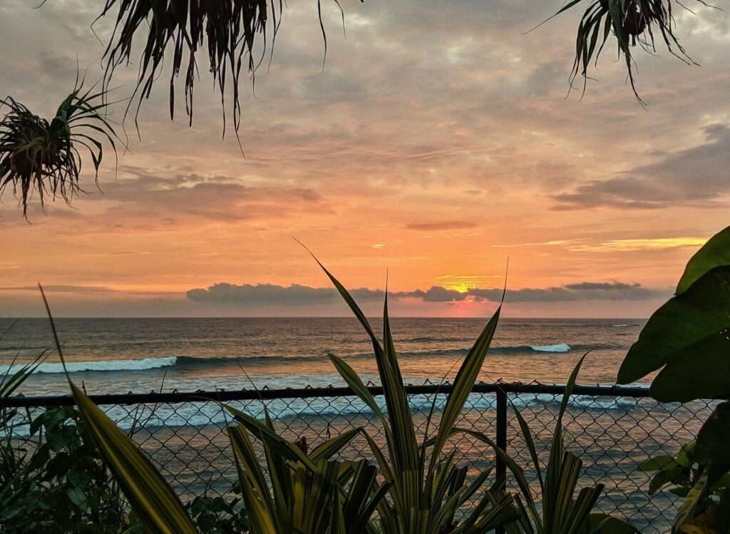 Beach view of small rolling waves at Weligama Surf Beach, Sri Lanka, with a stunning sunset casting a yellow glow across the sky