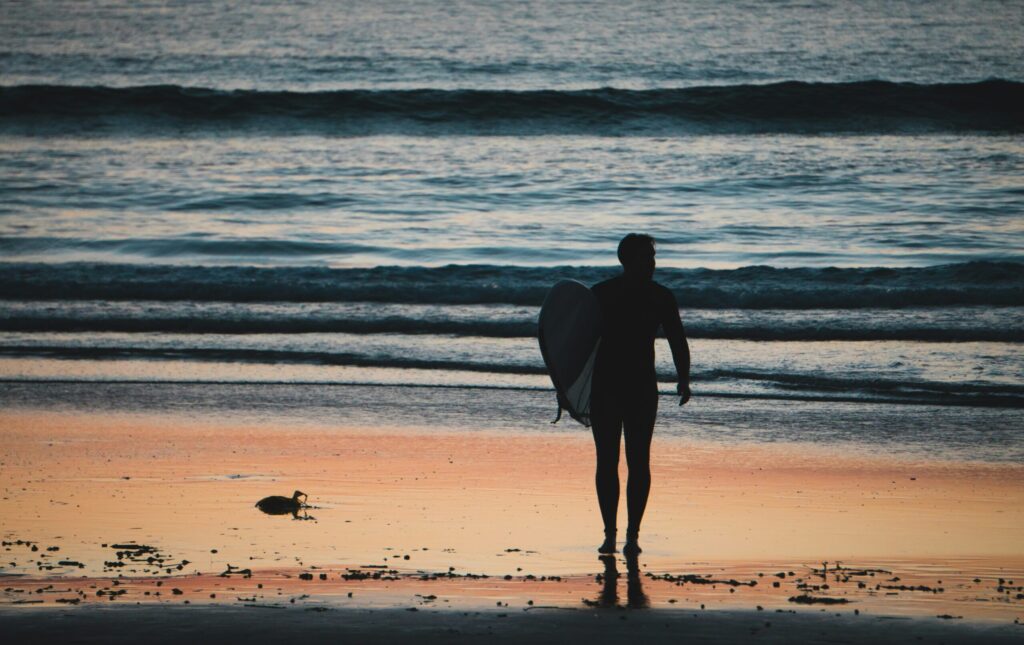 Surfer walking to Ayampe Surf holding a surfboard, low light and ocean in background