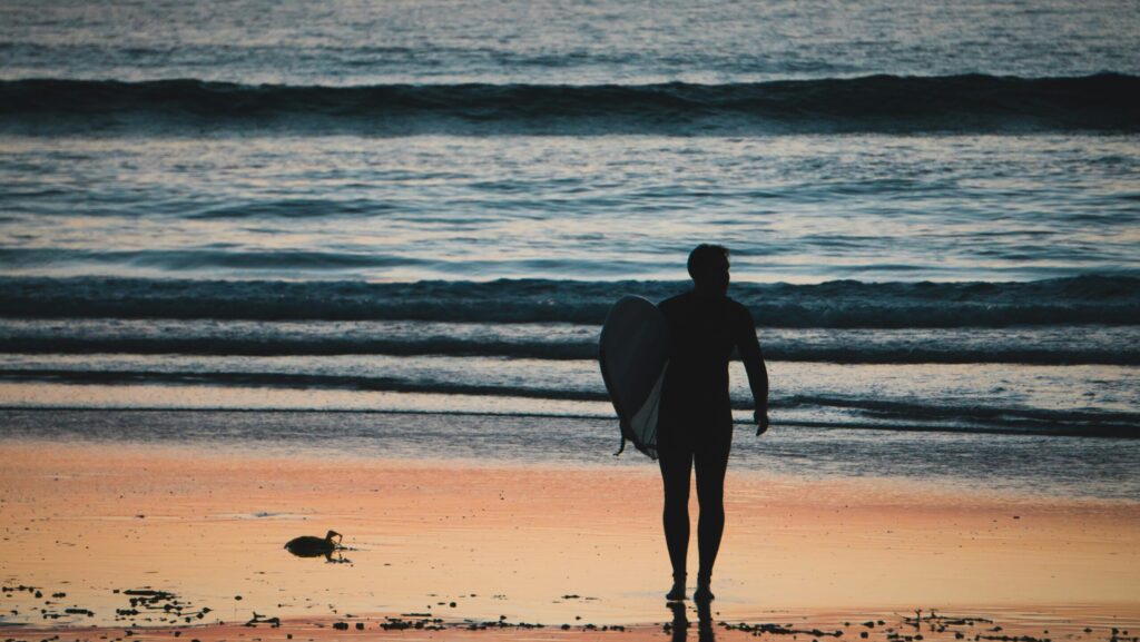 Surfer walking to Ayampe Surf holding a surfboard, low light and ocean in background