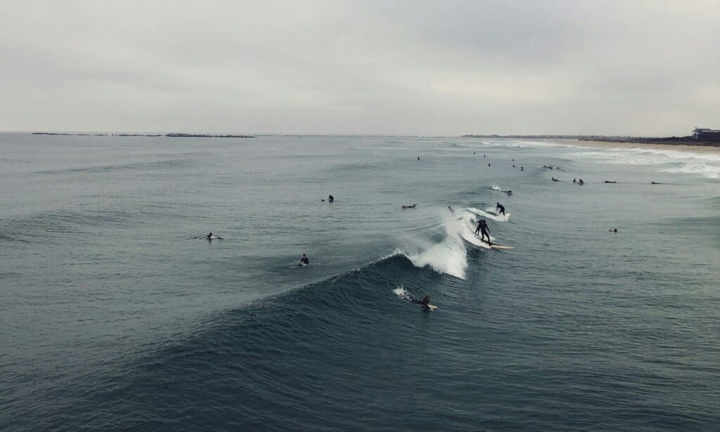 Surfers catching waves in deep blue water under cloudy skies, creating a dynamic and moody ocean scene