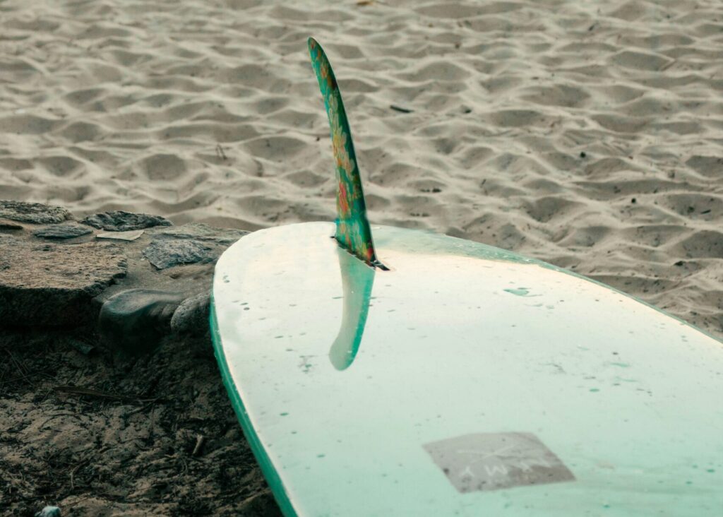 A single fin green Malibu surfboard resting on the sandy beach