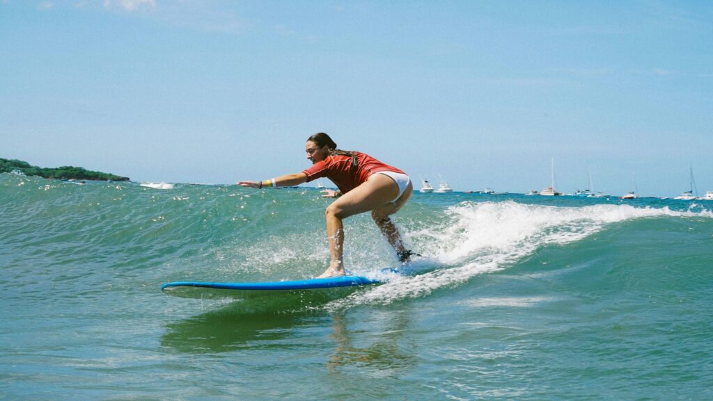 A girl learning to surf on a longboard in Tamarindo, Costa Rica surf, gliding on gentle waves in warm, clear blue water under bright blue skies