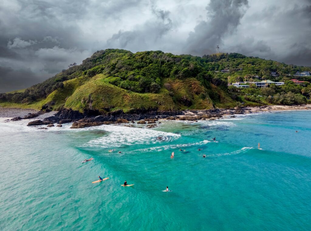 Aerial drone view of The Pass, Byron Bay Surf, featuring dark clouds above and bright blue water below