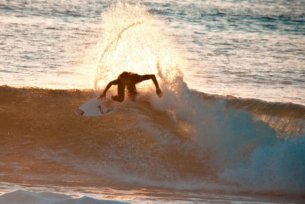 Surfer executing a backside turn on a wave, sending up a spray of water with sunlight glistening off the droplets