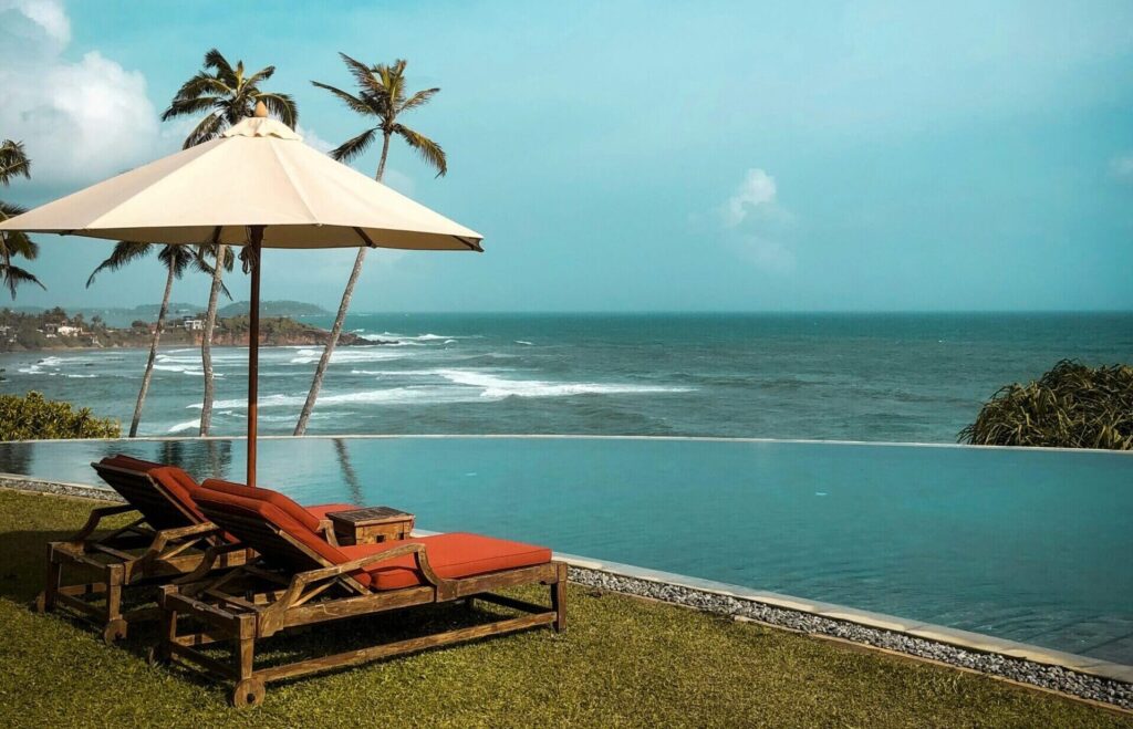 Two deck chairs with an umbrella facing the beach, with the sandy shore and ocean in the background at Weligama