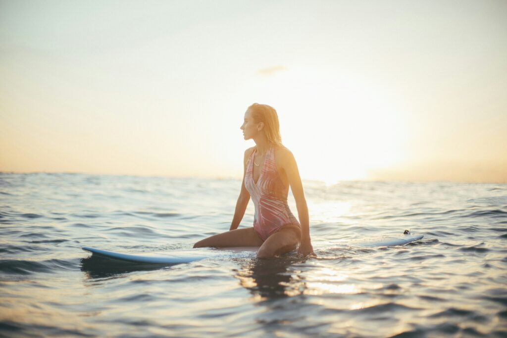 A blonde girl sitting on a longboard, enjoying the view as the sun sets in the background, creating a calm and peaceful atmosphere around her