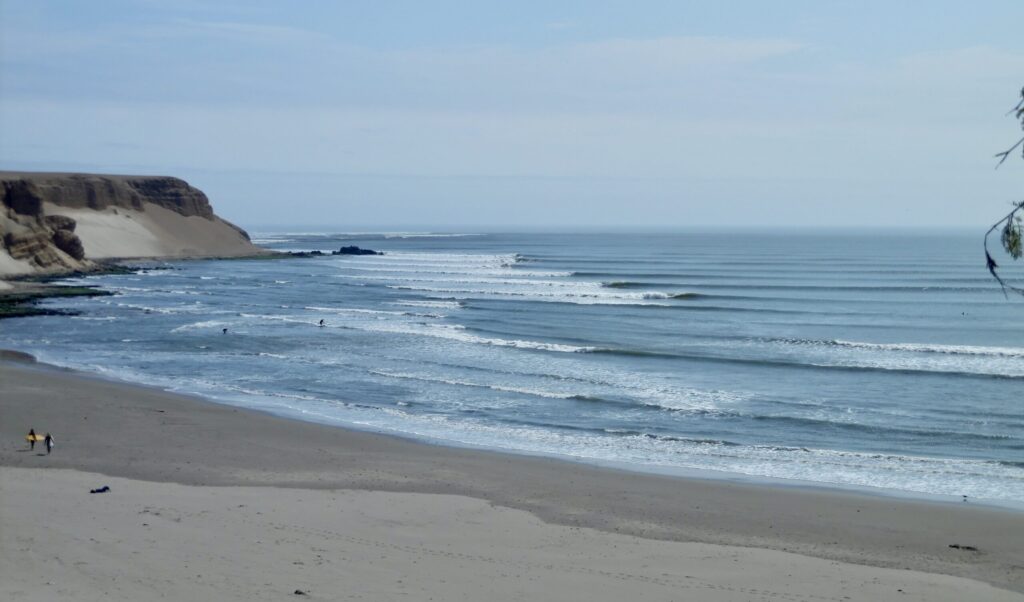 The long left-hand waves of Chicama surf in Peru, rolling endlessly under clear skies, with wave after wave peeling perfectly