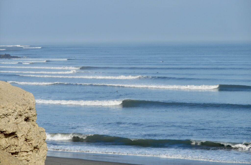 A long left-hand point break at Chicama surf, Peru, with perfectly peeling waves under clear skies and an empty lineup, little surfers in sight