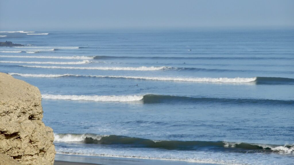 A long left-hand point break at Chicama surf, Peru, with perfectly peeling waves under clear skies and an empty lineup, little surfers in sight