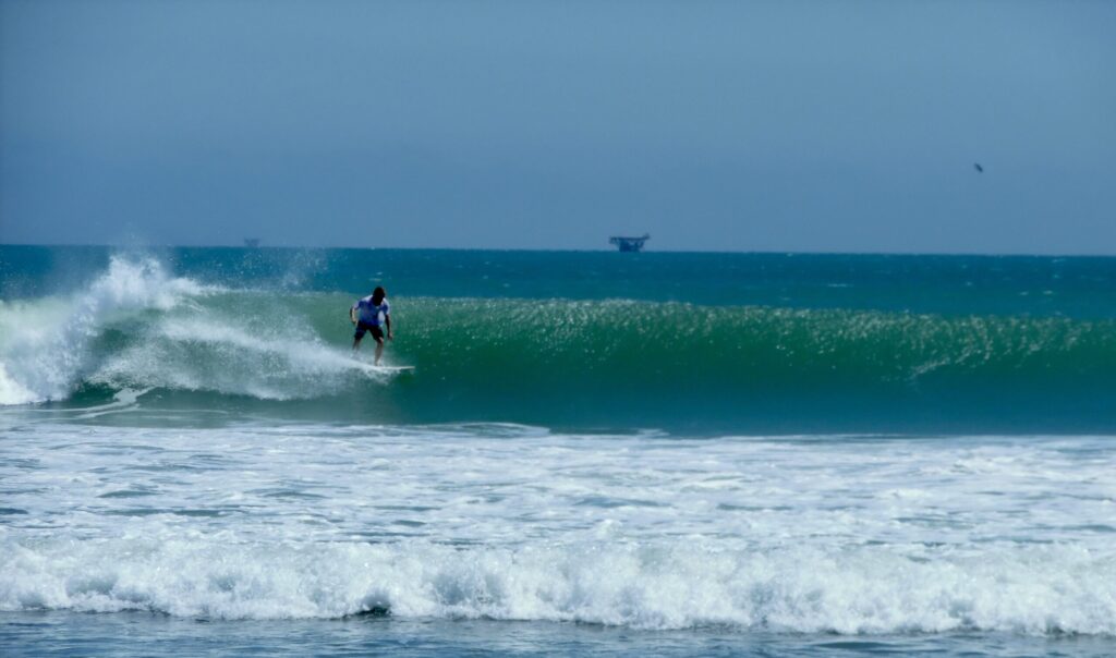 A surfer riding a left-hand break at Lobitos Surf Point, Peru, with blue skies and blue-green water surrounding the wave