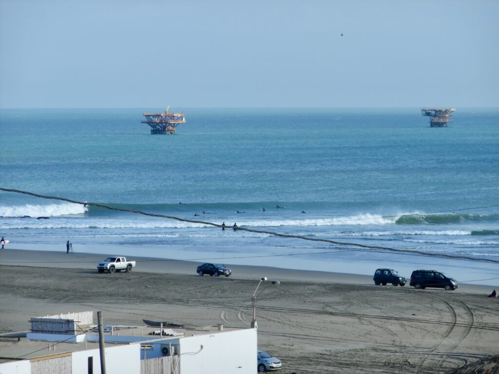 A big, long left-hand break at Lobitos surf Point, Peru, blue water and under blue skies, with two oil platforms visible in the background.