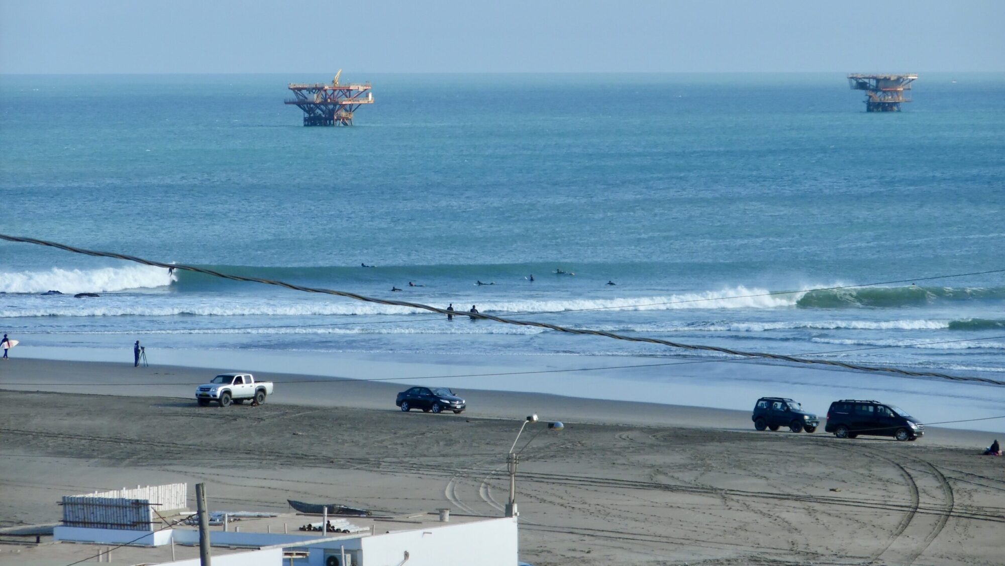 A big, long left-hand break at Lobitos surf Point, Peru, blue water and under blue skies, with two oil platforms visible in the background.