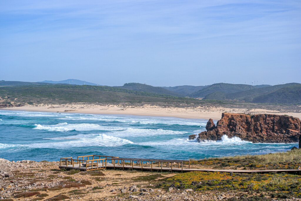 View from the lookout at Praia da Bordeira, featuring the ocean and rolling hills in the background under clear blue skies