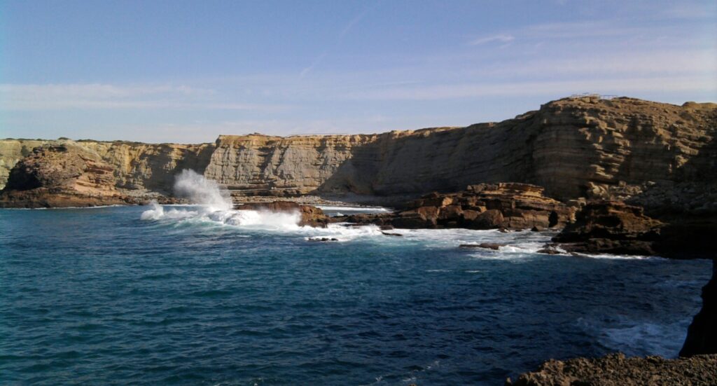 Ocean with cliffs in the background under clear skies in Carrapateira, Algarve