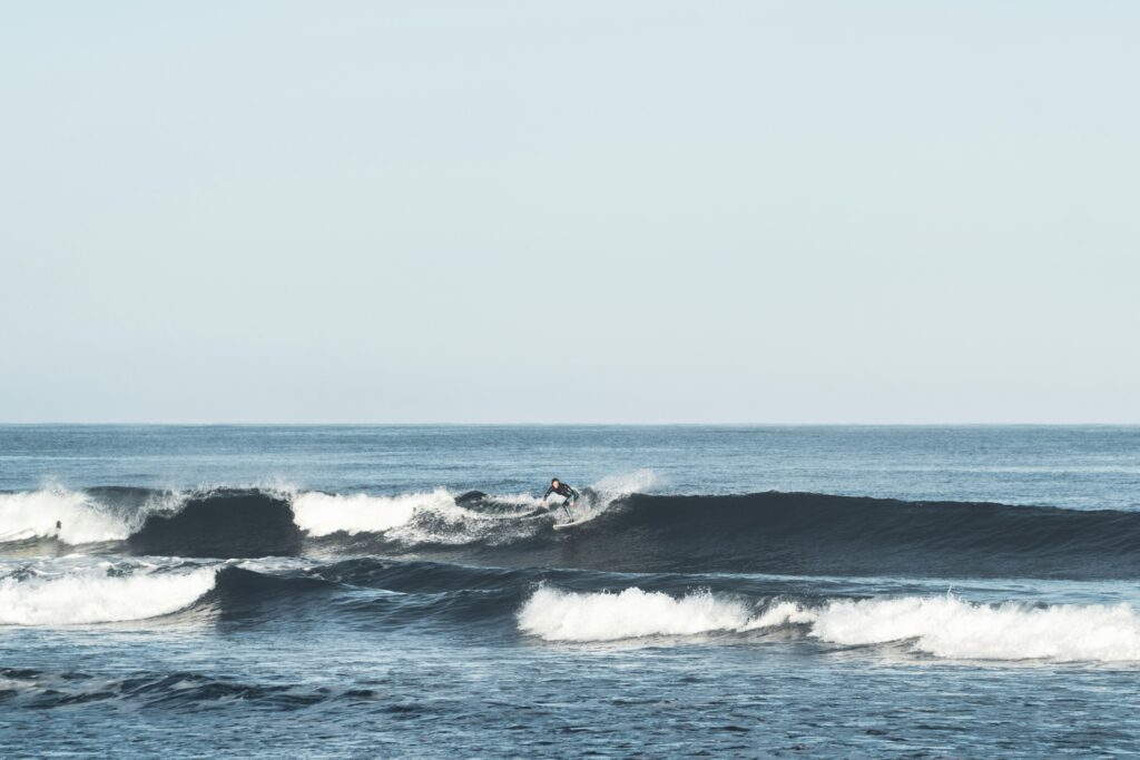 A surfer executes a dynamic backside turn on a clean left-hand wave, sending a spray of water in Cadiz Surf, Spain