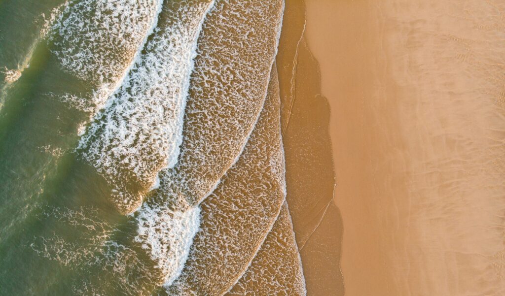 A bird's-eye drone view of rolling right-hand waves breaking over golden sand in Lacanau Surf, France