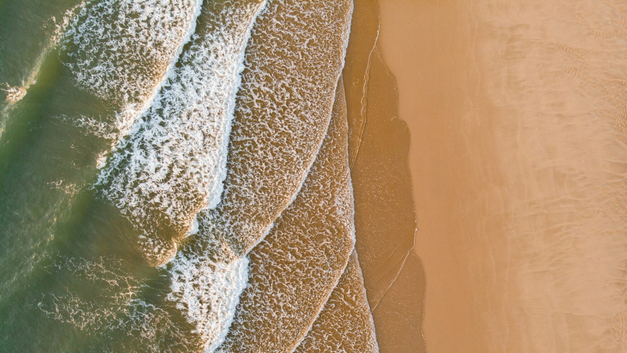 A bird's-eye drone view of rolling right-hand waves breaking over golden sand in Lacanau Surf, France
