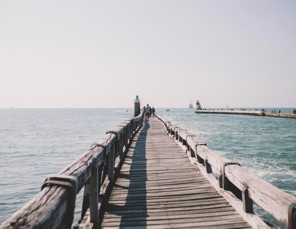 Estacade Pier in Capbreton stretches into the ocean, flanked by water on both sides, set against a backdrop of clear blue skies