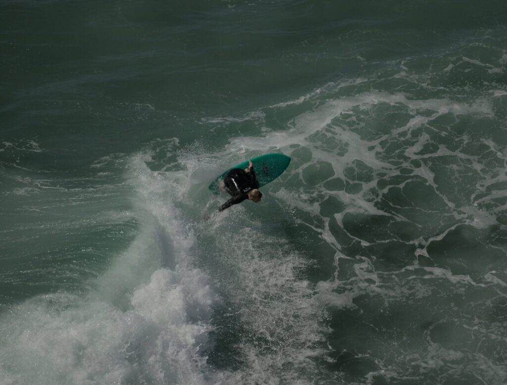 A surfer performs a backhand floater on a green surfboard, gliding over a wave with vibrant green-blue water at Huntington Beach surf, California