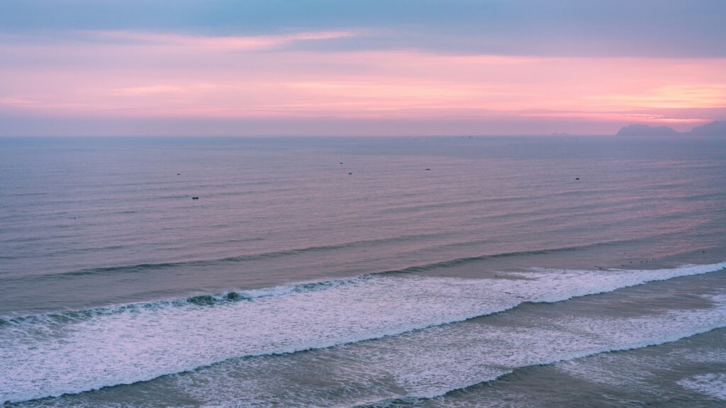 Makaha Beach, Miraflores surf in Lima, featuring rolling waves under a stunning sky painted with shades of orange and purple