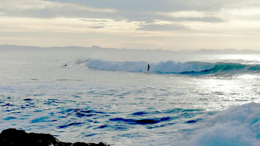 A surfer riding a wave in Capbreton surf, France, with light reflecting off the ocean's surface under cloudy skies