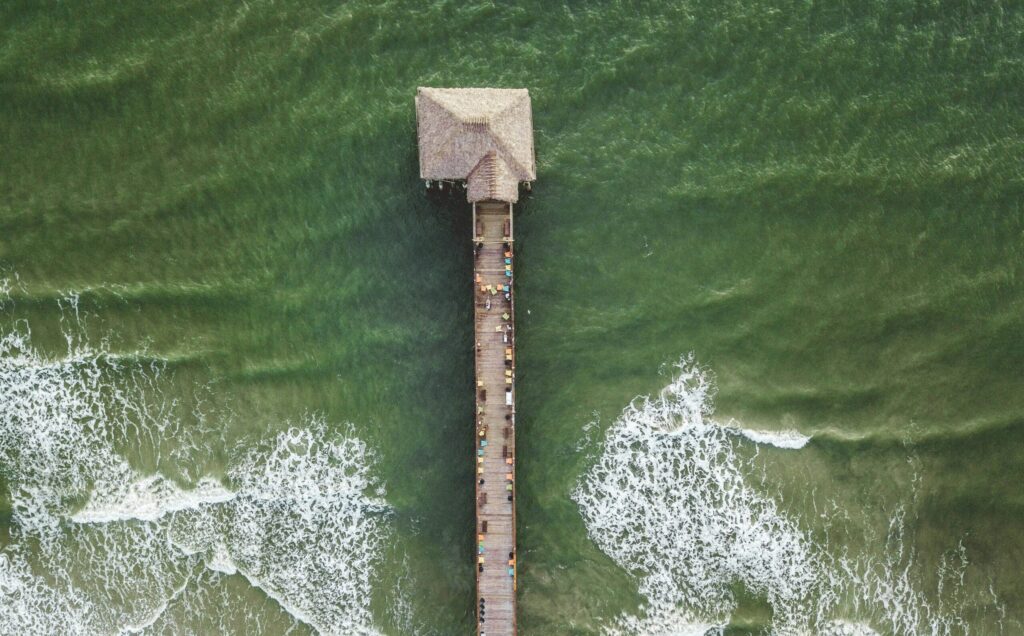 A drone shot from above of Cocoa Beach surf Pier, Florida, highlighting the green-blue water below and the vibrant beach atmosphere