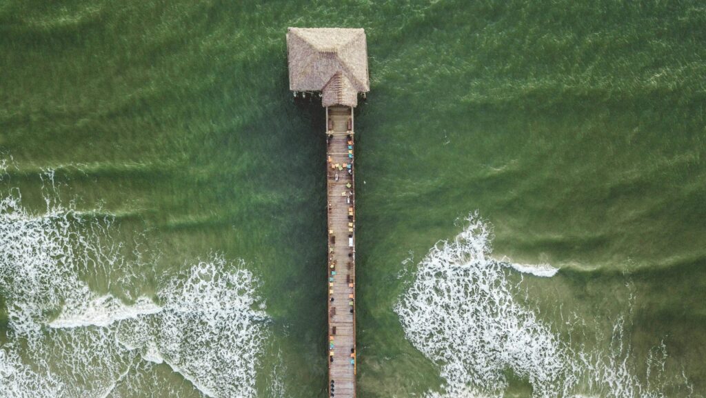 A drone shot from above of Cocoa Beach surf Pier, Florida, highlighting the green-blue water below and the vibrant beach atmosphere