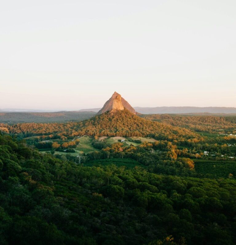 Sunrise over Mt. Ngungun in the Glass House Mountains, casting golden light on rolling green hills and lush trees