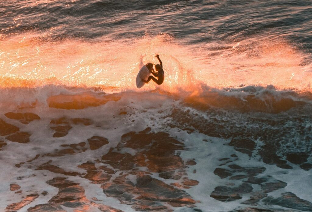 Surfer executing an air move with sunlight reflecting off the water and spray flying around in Ribeira d'Ilhas, Ericeira surf